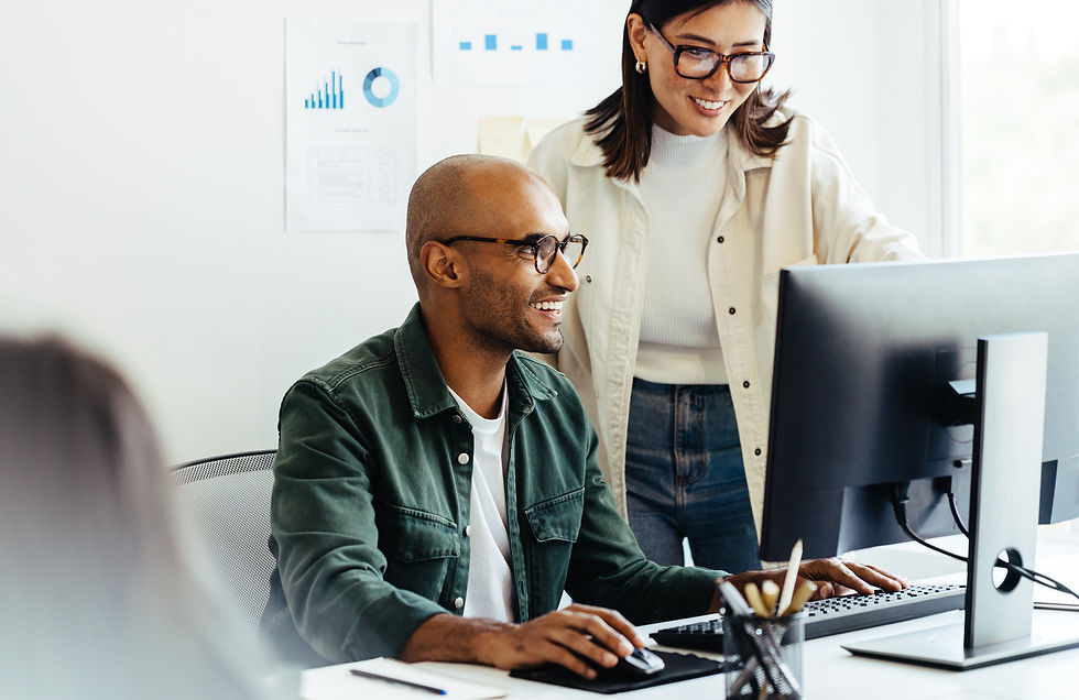 Two colleagues smiling and collaborating while working on a desktop computer in a professional office environment