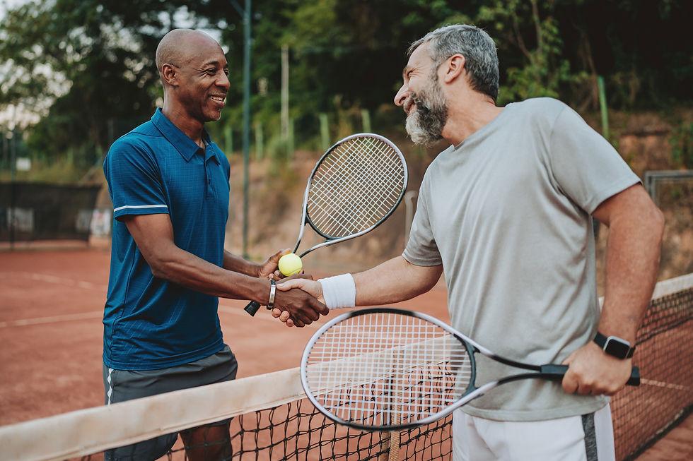 Two men shaking hands at the net after a tennis match, holding their rackets and smiling.