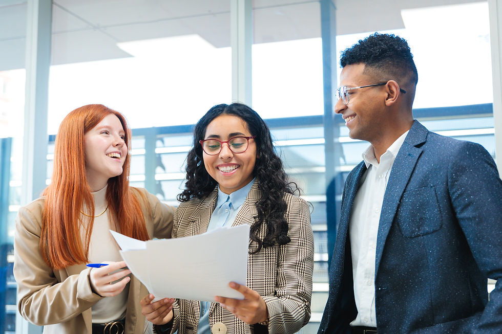 Three smiling colleagues reviewing documents together in a bright office space.