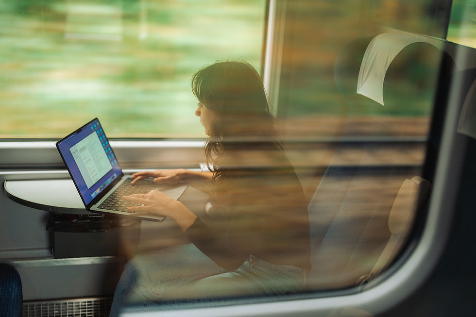 A woman working on her laptop during a train journey, with a blurred scenic view outside the window