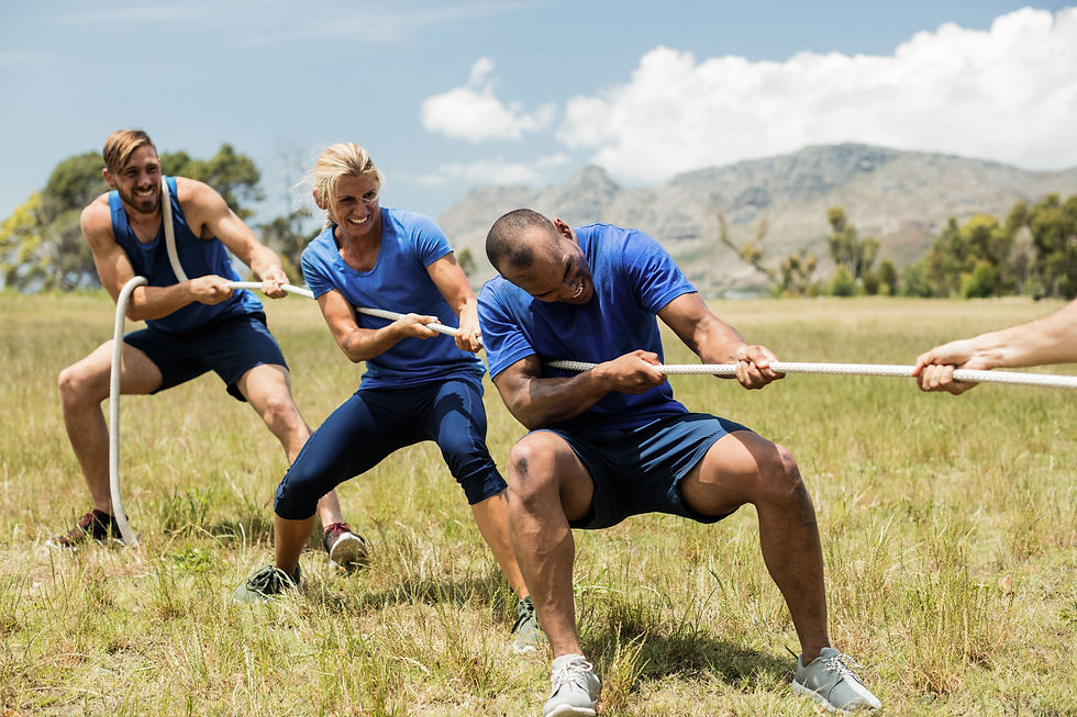 Three people in blue shirts pulling a rope in a competitive outdoor tug-of-war event.