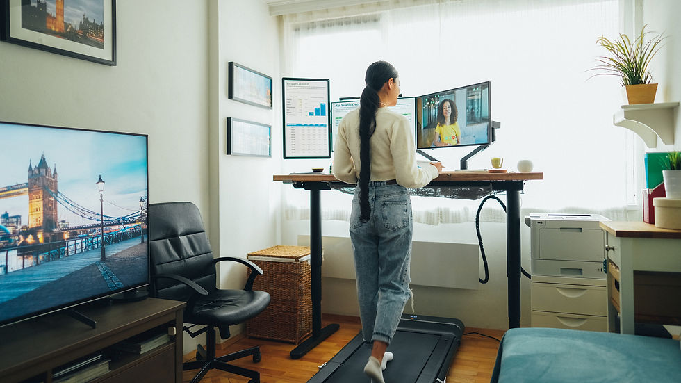 A woman walking on a treadmill desk while working on multiple monitors in a bright home office