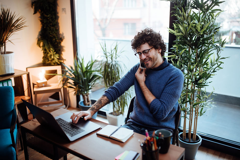 Smiling man working on a laptop in a cozy, plant-filled home office.