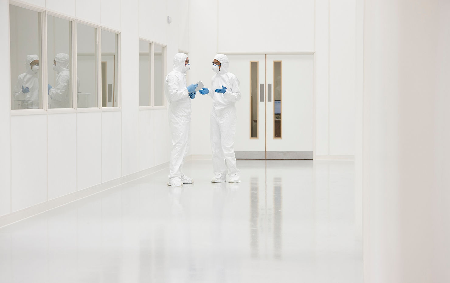 Zwei Mitarbeiter tragen die vorgeschriebene Reinraumkleidung in einem Reinraumumfeld und unterhalten sich