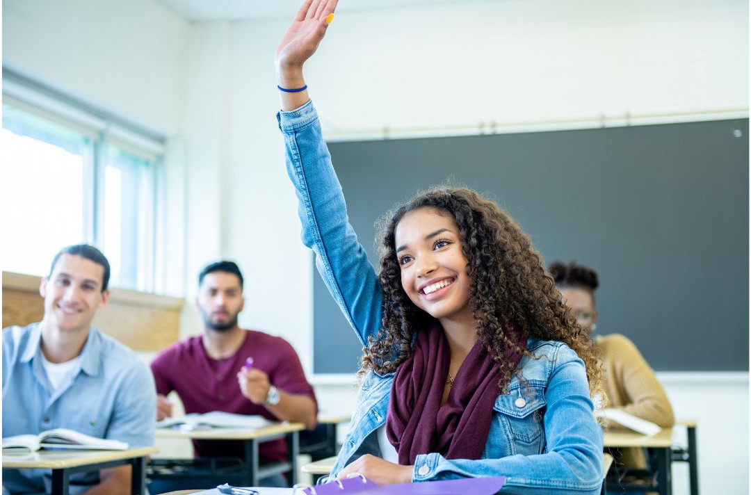 Teen student raising her hand in class to speak up and participate.