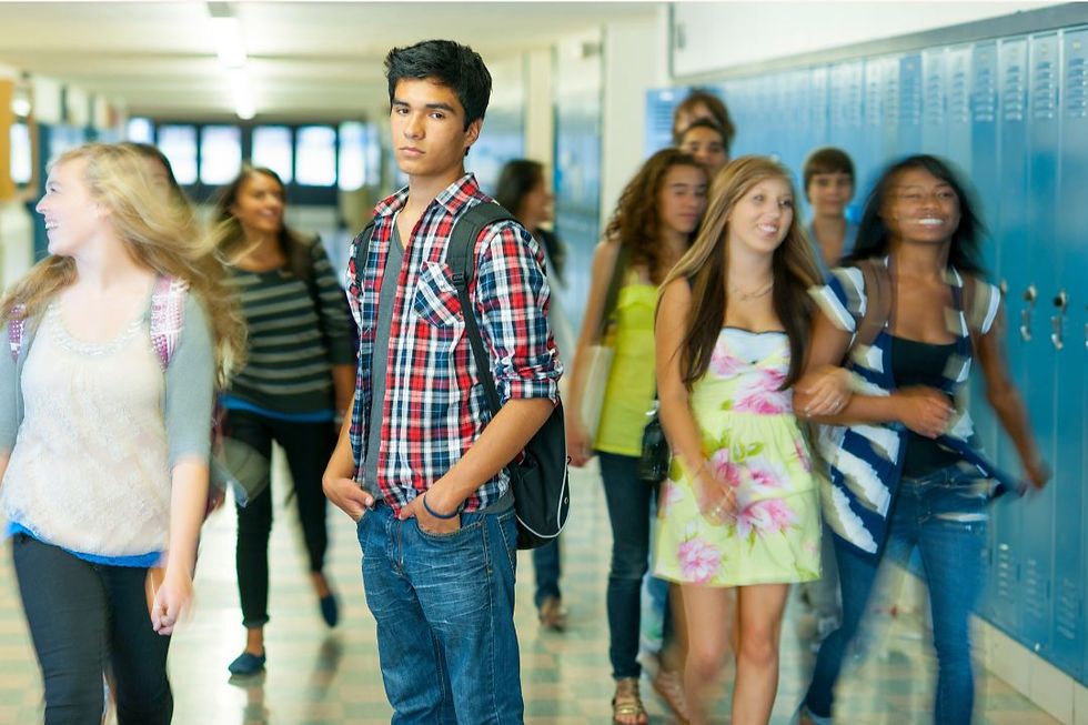 A high school student standing in a hallway while other students walk by, representing changing friendships and social navigation in high school.