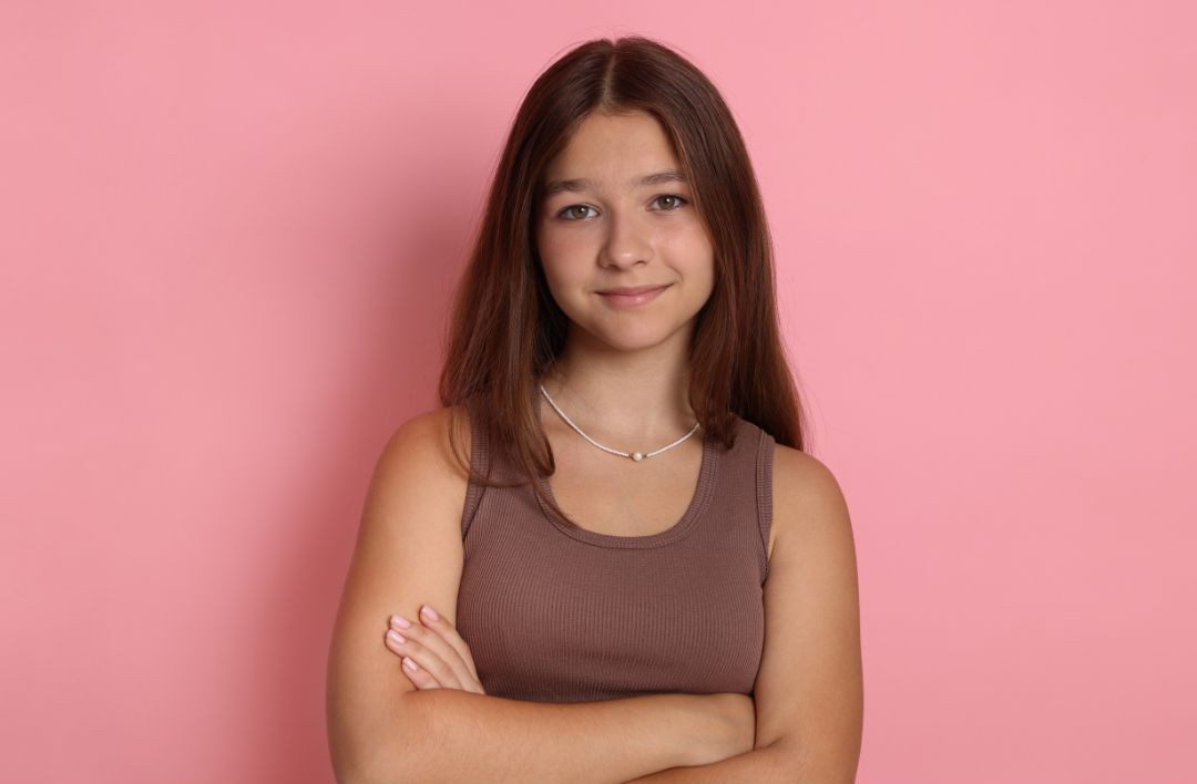 Confident teenage girl standing with arms crossed and a calm smile.