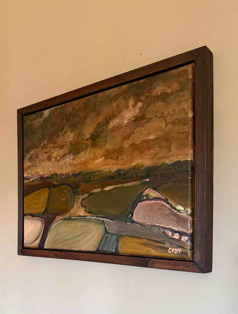 a framed painting of a landscape hung on a white wall
