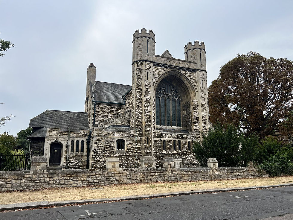 Stone church with tall arched window, flanked by trees and a stone wall. Overcast sky creates a serene and historic mood.