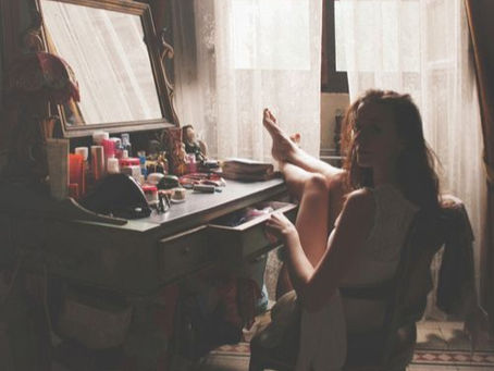 Woman sitting at a vanity during her morning skincare routine in natural window light.