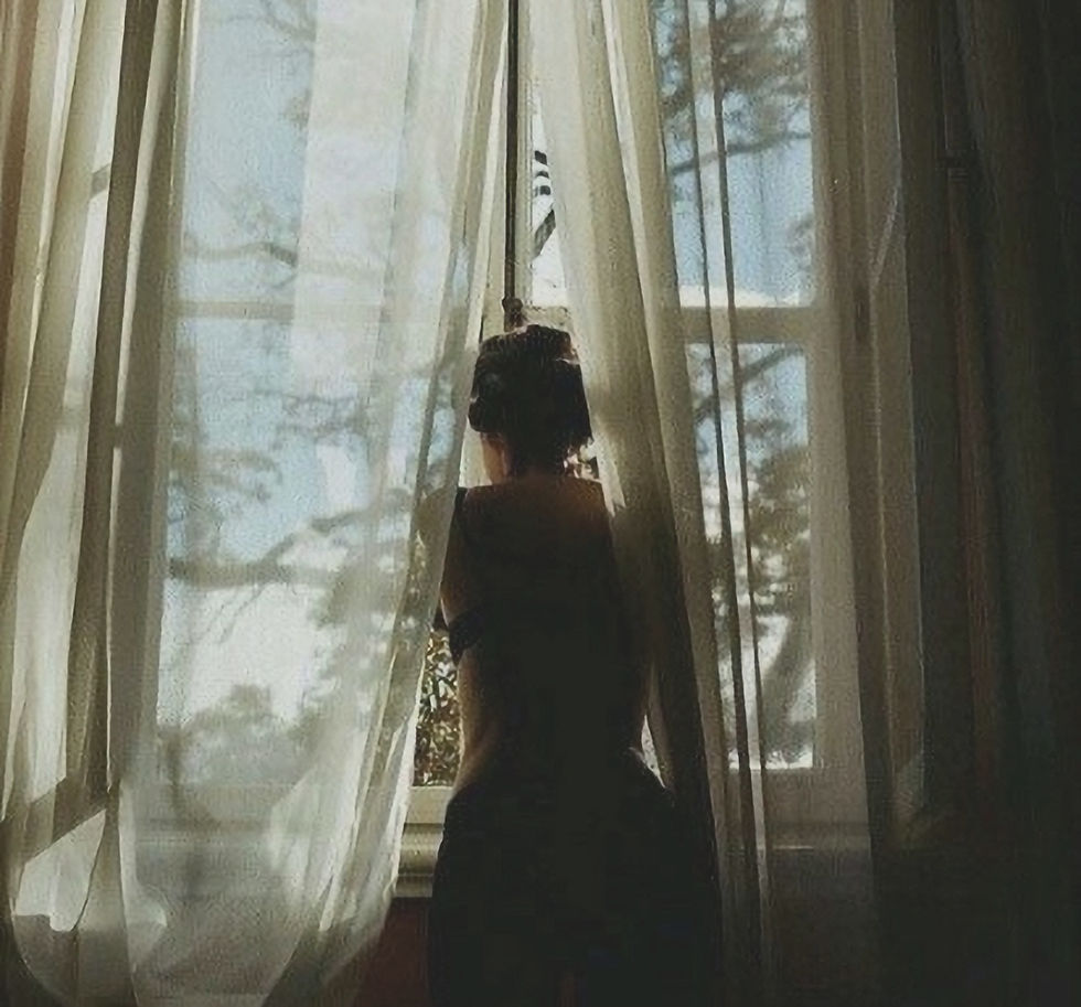 Woman standing by a window in soft morning light, reflecting on creating a peaceful life.