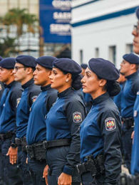 Fileira de policiais de uniforme azul e boina, em posição de sentido, durante formatura ao ar livre.