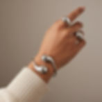 Hand wearing silver rings and bracelet, neutral background, accessories.