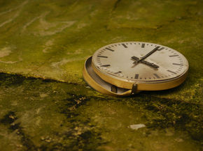 Broken clock lies on a mossy, green surface. The clock face evokes a sense of neglect and decay.