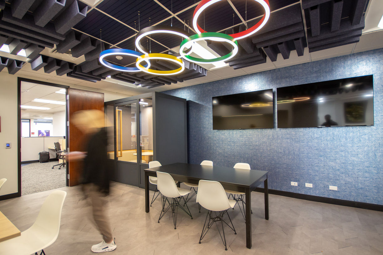 Open break area with small tables and chairs, wall-mounted screens, and a black exposed ceiling with modern lighting.