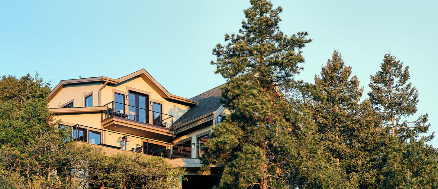 Exterior view of a multi-level home integrated into a wooded hillside with pine trees and layered decks.