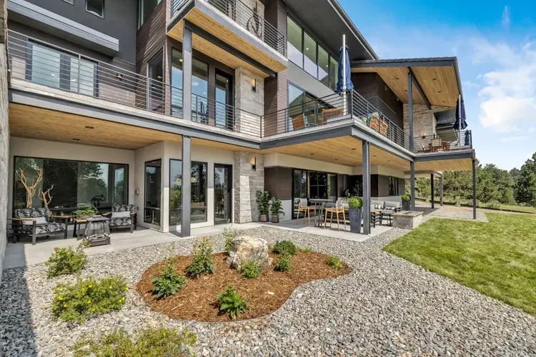 Exterior view of modern mountain home with balconies, stone, and wood materials on a sloped site.