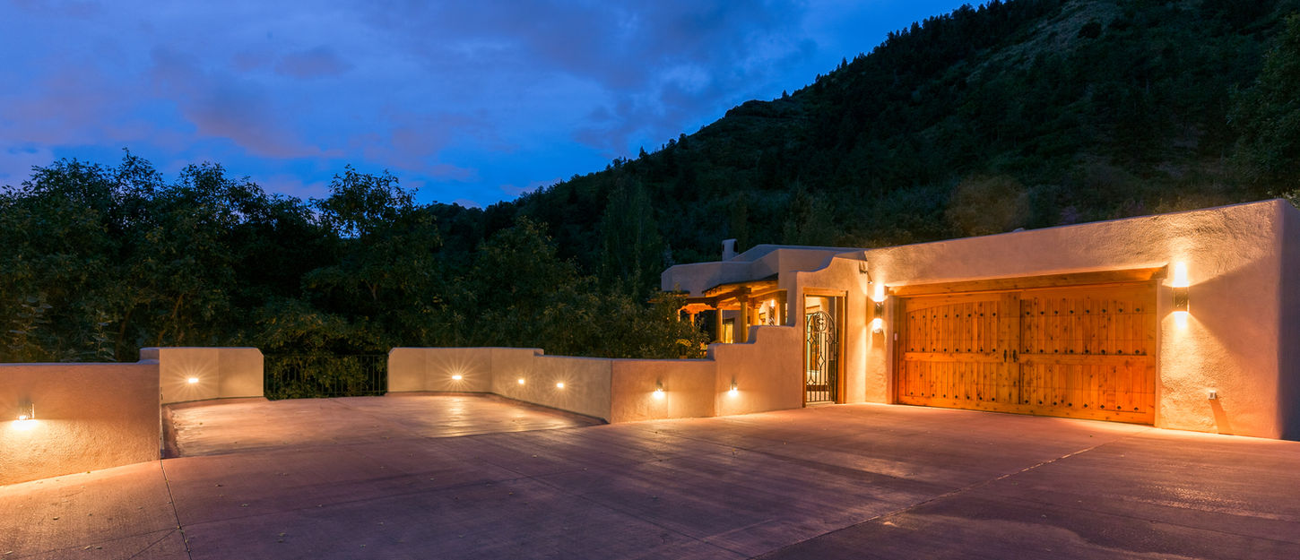 Evening view of a renovated home in Manitou Springs with warm exterior lighting, stucco walls, and a covered parking area.