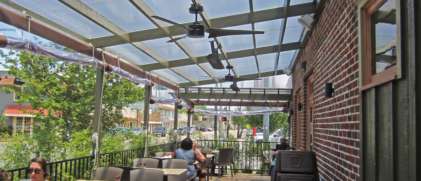 Outdoor dining area with translucent sun shades, landscaped surroundings, and brick façade.