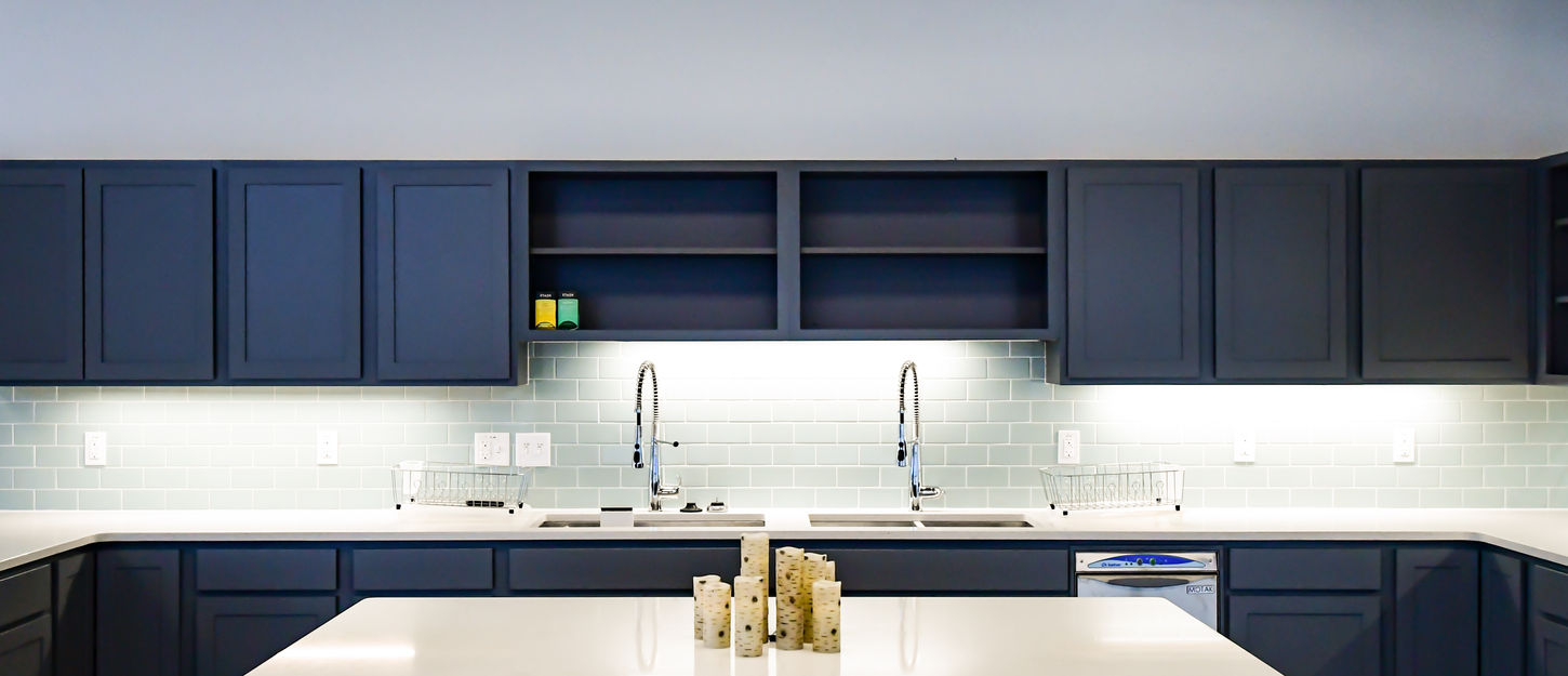 Community kitchen with dark blue cabinets, white island countertop, tile backsplash, and exposed ductwork.