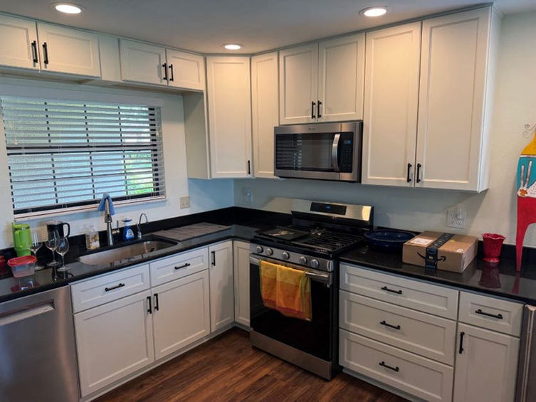 white kitchen counters with black pull handles a black oven and stainless steel microwave and dishwasher