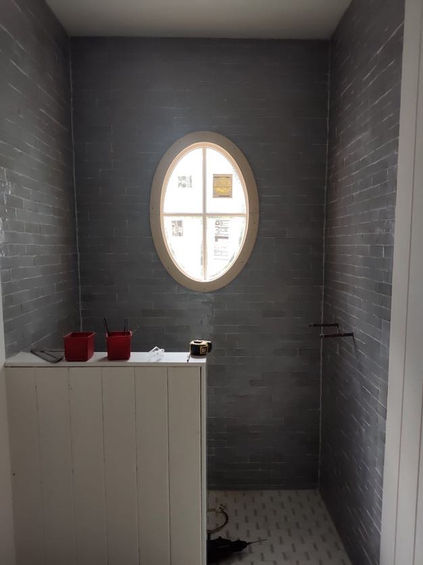 thin gray tiles around a half wall with an oval window and sunlight peering through
