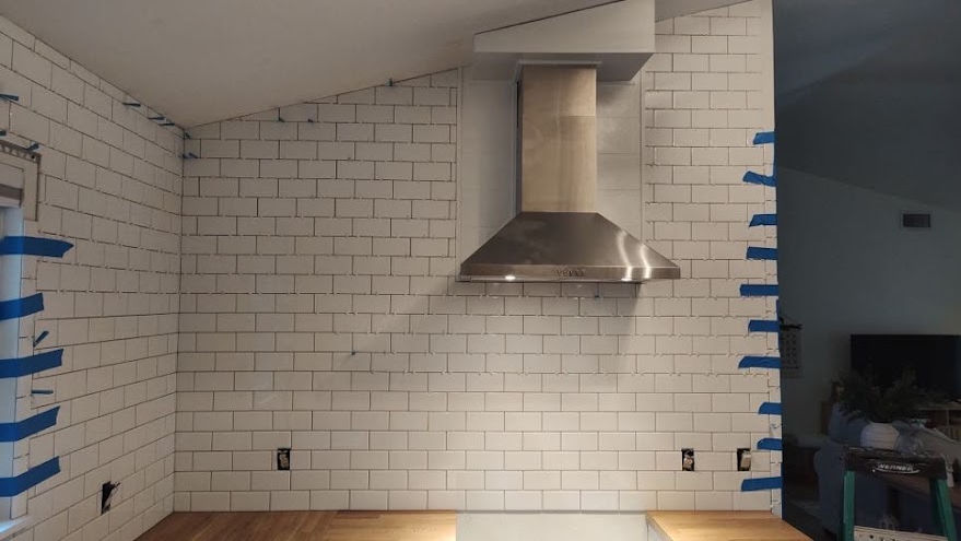 Remodeled kitchen with white back splash tile and a metal range hood