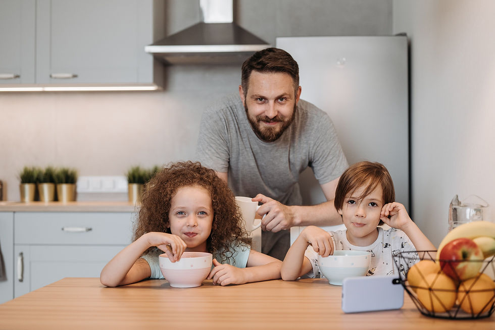 a man standing behind two small children sitting at a table and eating