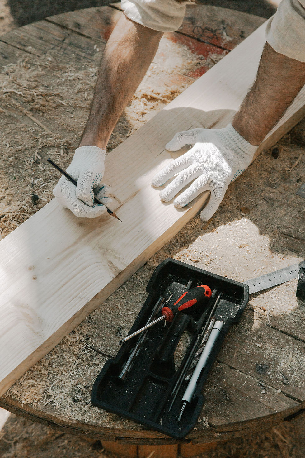 construction worker marking on a piece of wood with a tool box and screwdriver next to him