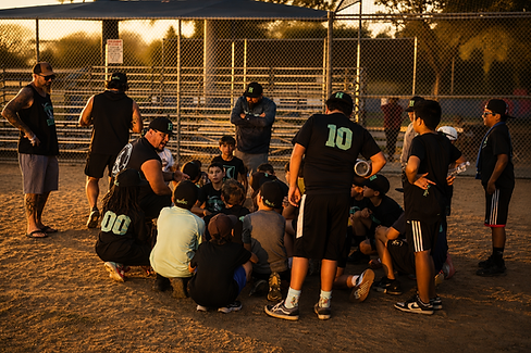 Coaches huddle with youth baseball team at sunset