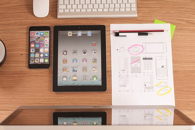 A phone, a tablet, and a notepad in front of a computer monitor.