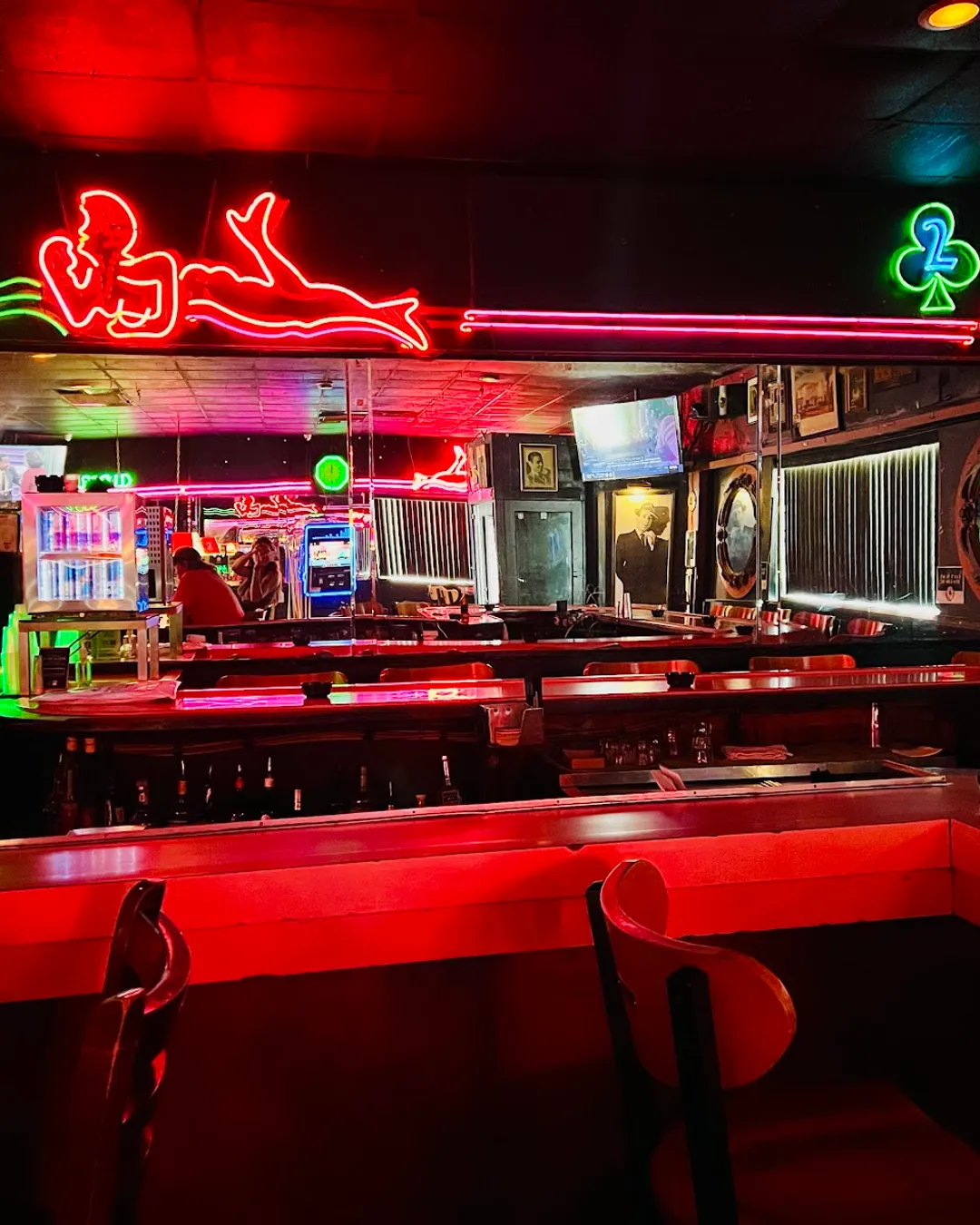 Mac's Club Deuce legendary pink curved bar and Beloved Neon Lady. The pink neon figure is surrounded by green and pink neon stripes. A mirror shows the reflection of another mirror from across the bar.