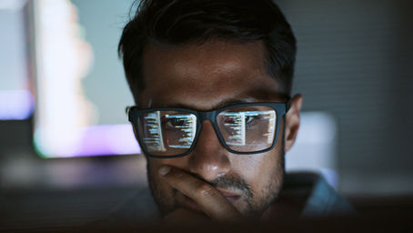 A developer looking at code with monitor reflecting in glasses