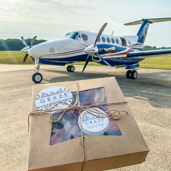 Hand holding KRAZE box, small private airplane on airfield background.