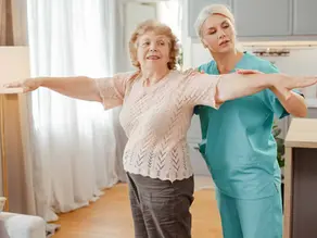 Physiotherapist supporting an older woman with arm balance exercises during stroke rehabilitation at home