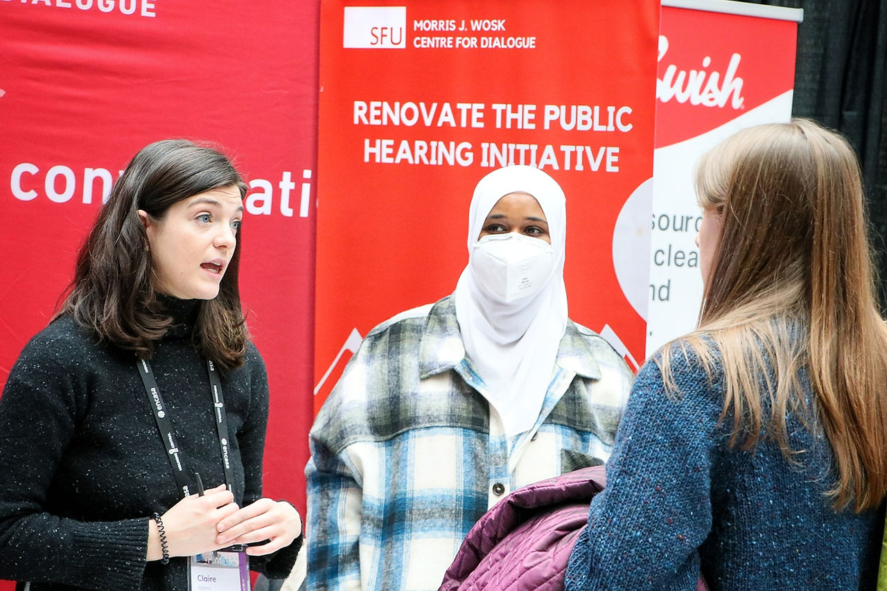 RPHI's Claire Adams and Ayaan Ismail speak with a booth attendee, RPHI standup banners are seen in the background