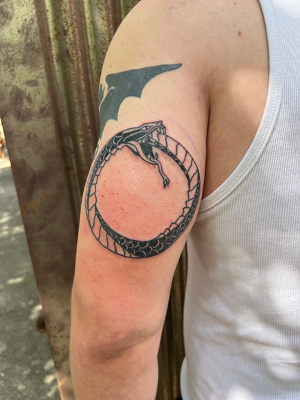 Tattoo of snake eating its tail.  Circle shaped.  Upper left arm bicep.