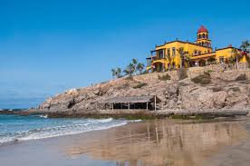 Beach of Todos Santos with rocky hill on the side, that has a yellow building on top. 