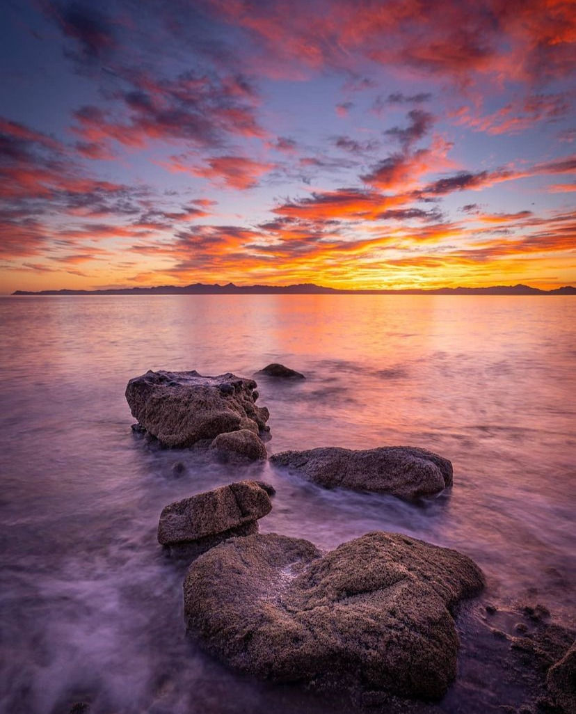 Sun setting on the Bay of Loreto, with small waves crashing on rocks close to the shore.
