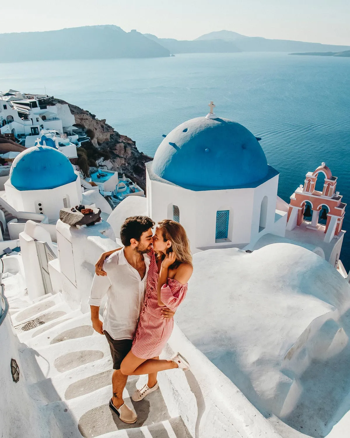 Couple sharing a kiss on their honeymoon in Santorini with the iconic architecture behind them.