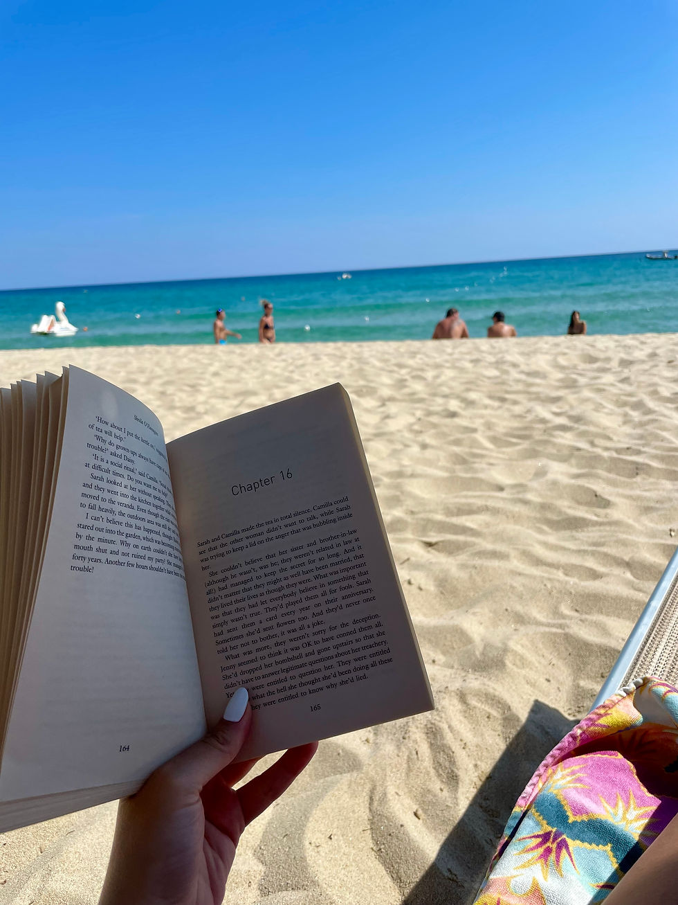 Woman holding a book at the beach with the ocean in the background.