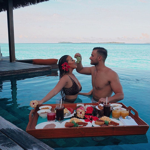 Couple sharing a tray of food in a pool overlooking the ocean on their honeymoon in the Maldives.