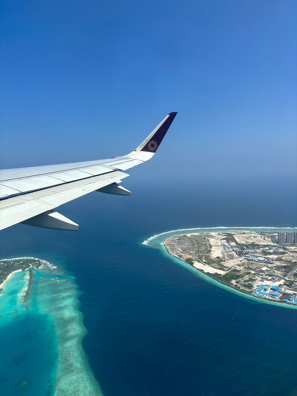 View out of an airplane window, where you can see the sing of the plane over a body of water and a small strip of land.