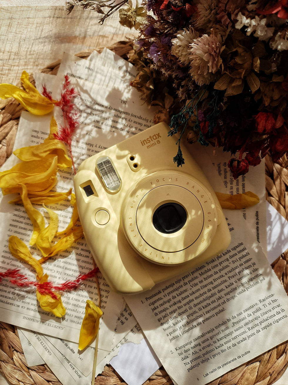 Instax instant camera surrounded by book pages and flowers.