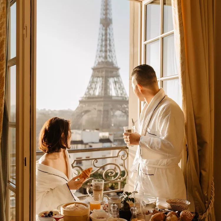 Couple enjoying breakfast on the balcony of their hotel room overlooking the Eiffel Tower. 