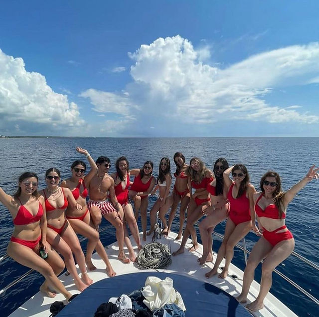 Bridal party dressedin red bikinis and the bride in white posing on a yacht in Playa del Carmen. 