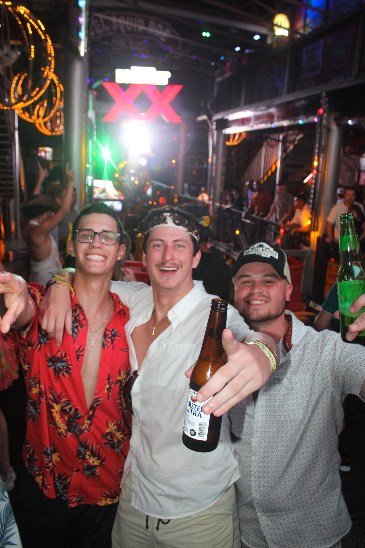 A group of 3 guys posing with their beers at El Squid Roe, in  Cabo, Mexico. 