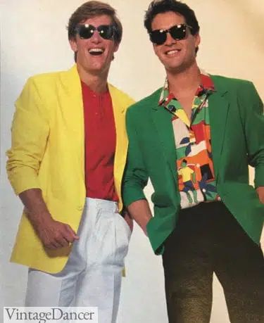 Two men with sunglasses, one wearing a colorful button-up shirt with a forest green jacket and black pants, the other with a red button-up shirt paired with a bright yellow jacket and white pants. 
