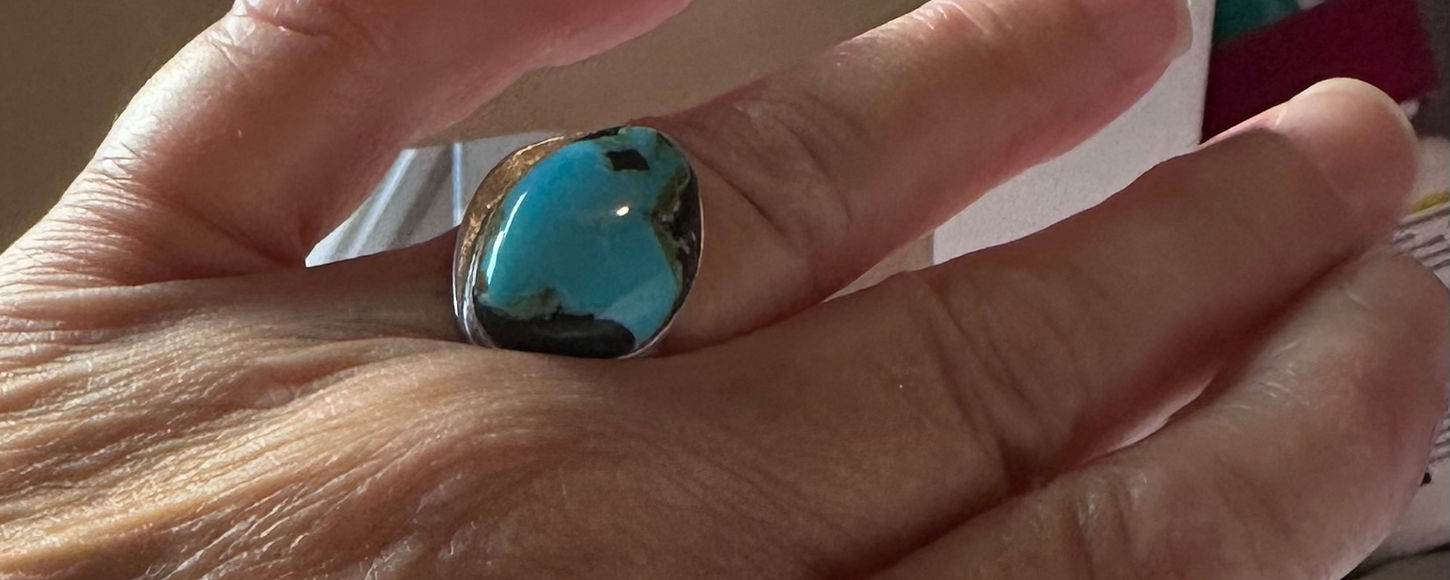 A very large turquoise ring being worn on woman's left hand held up in front of window.