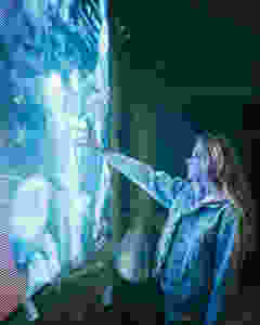 Woman in urban clothing touching a large, blue artificial screen.